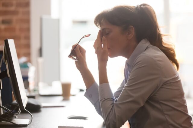 Tired woman at a computer desk holding her glasses